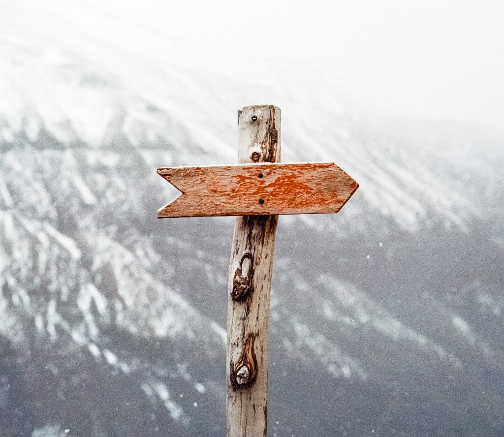 Ein Holzschild steht auf einem Stab vor einem Berg. Das Schild zeigt als Pfeil nach rechts, hat aber keine Aufschrift.
