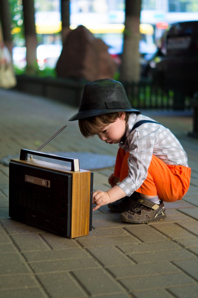 Ein kleiner Junge sitzt vor einem alten Radio und drückt auf einen Knopf.
