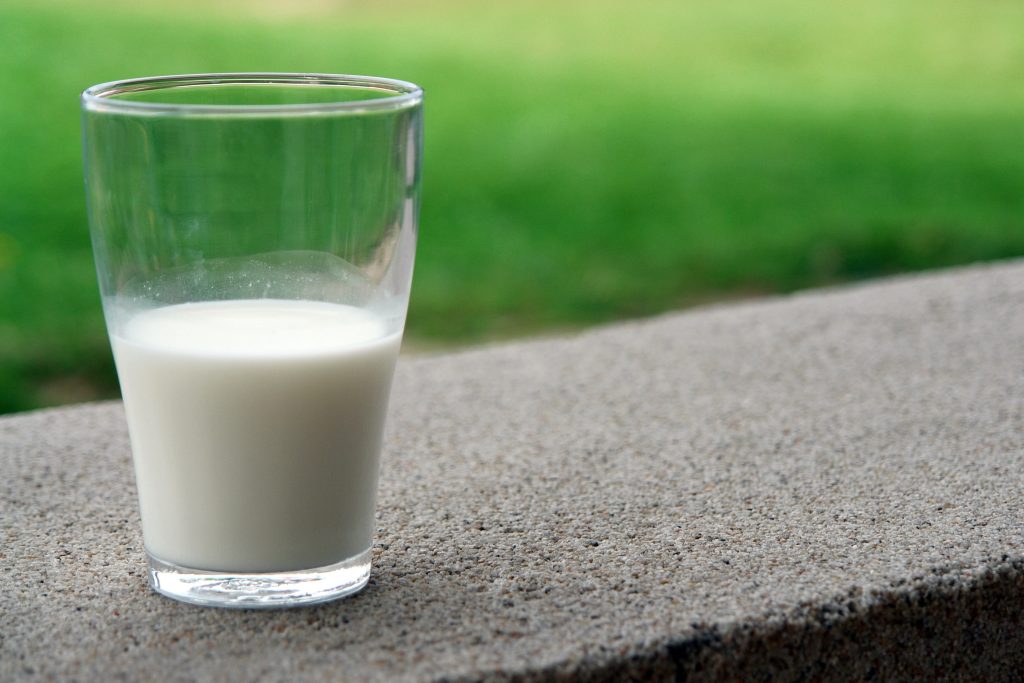Ein halb volles Glas Milch vor einem grünen Rasen.