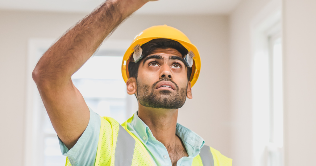 Ein Mann mit Warnweste und Bauarbeiter-Helm schaut analysierend zur Decke. Zu einem Blog über Arbeit-Fails.