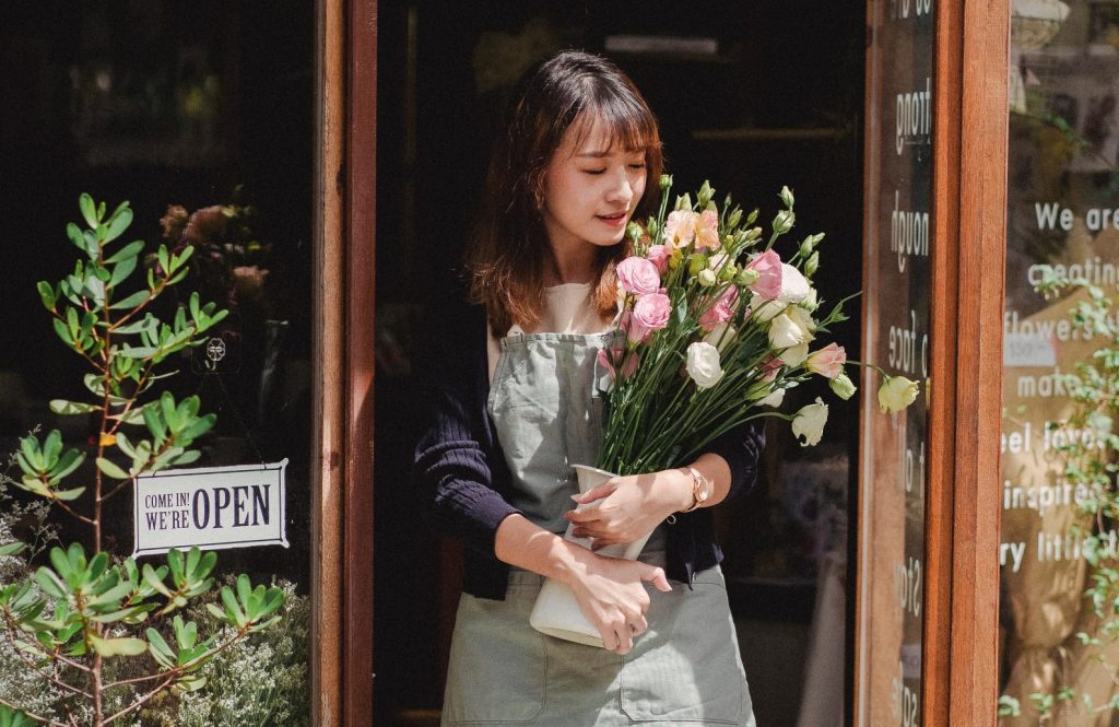 Eine Frau kommt mit einem Blumenstrauß aus einem Blumenladen.