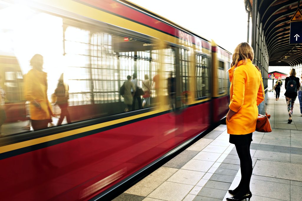 Eine Frau steht an einem Bahnsteig an dem ein rot-gelber Zug schnell vorbeifährt. Es gehört zum Artikel der Bahnposts der Woche.