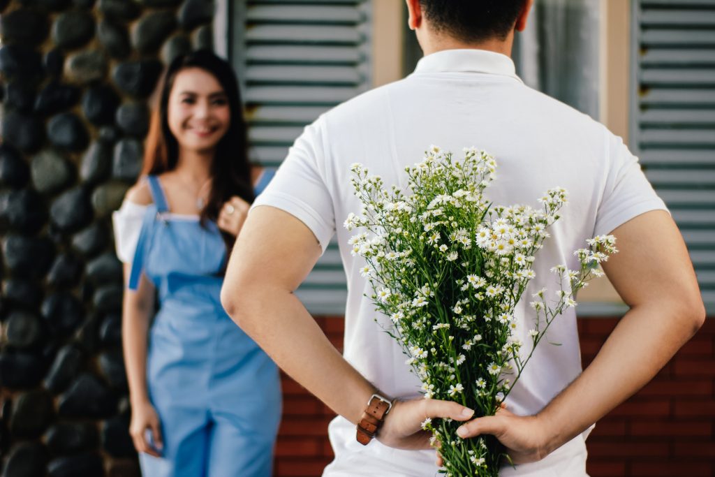 Ein Mann hält einen Blumenstrauß hinter seinem Rücken, um die Frau, die ihm gegenüber steht, zu überraschen.